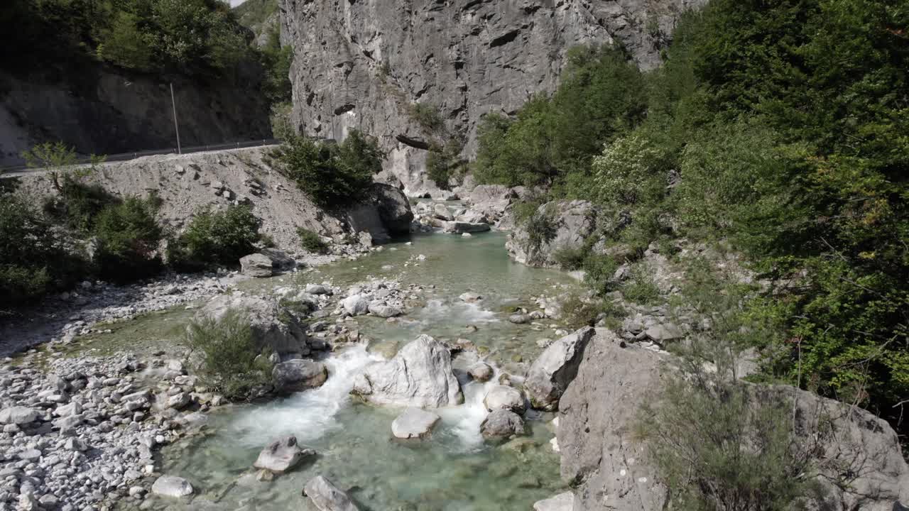 video de drone de un avion grua ascendiendo unos metros sobre el rio valbone desde, video muy cerca del agua, se puede ver el agua cristalina azul turquesa rompiendo entre las rocas