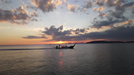 Barco-Tradicional-Navegando-A-Alta-Velocidad-Por-El-Mar-Con-Una-Hermosa-Puesta-De-Sol-Justo-Encima-De-Las-Siluetas-Del-Paisaje-Montañoso-De-Krabi