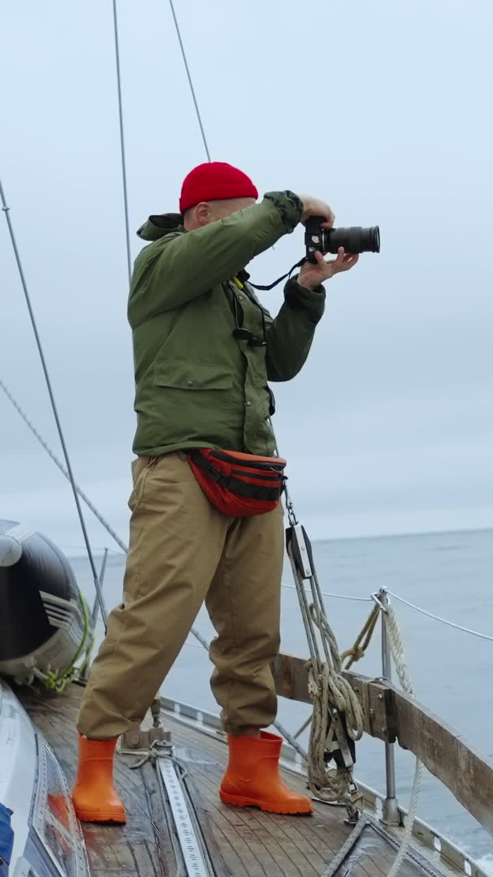 Homme en bonnet rouge prenant des photos sur un voilier
