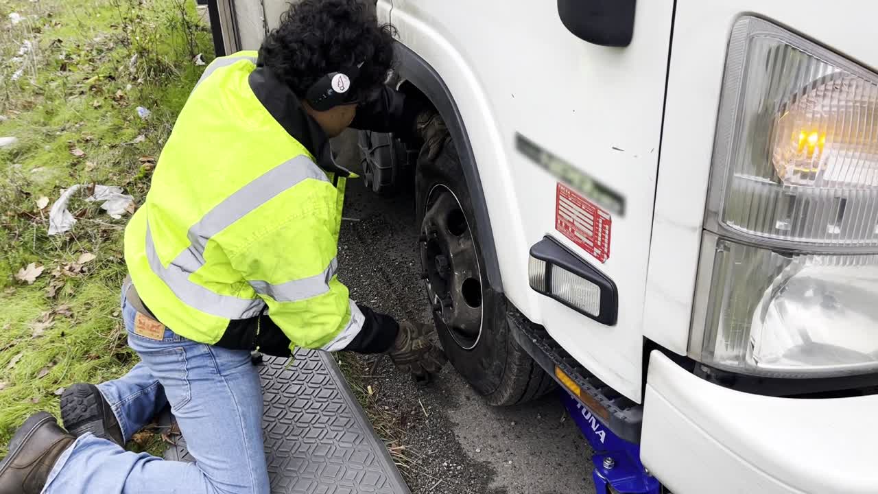 Homem hispânico trocando o pneu de um reboque parado na estrada