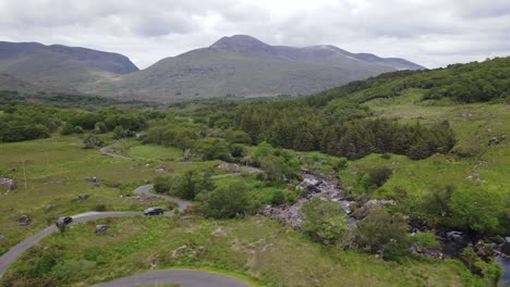 winding rural road with cars passing in the mountain valley with black river stream following the road