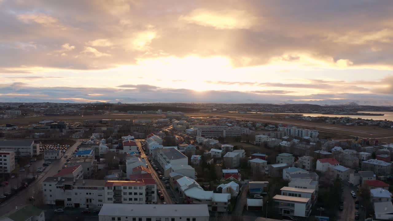 Drone in volo sopra le case e i tetti di Reykjavík per rivelare il sole che risplende tra le nuvole durante un magnifico tramonto, ripresa aerea ascendente