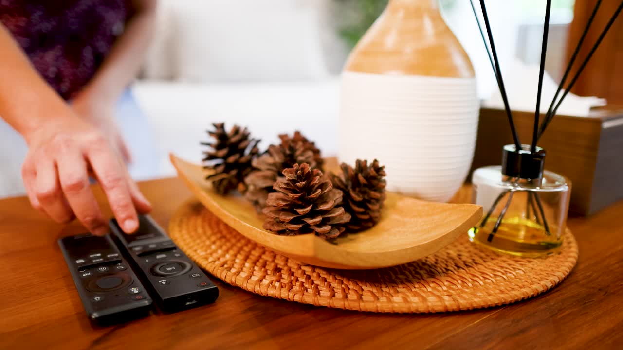 Une main tendue vers une télécommande de télévision sur une table en bois avec des accessoires de décoration intérieure
