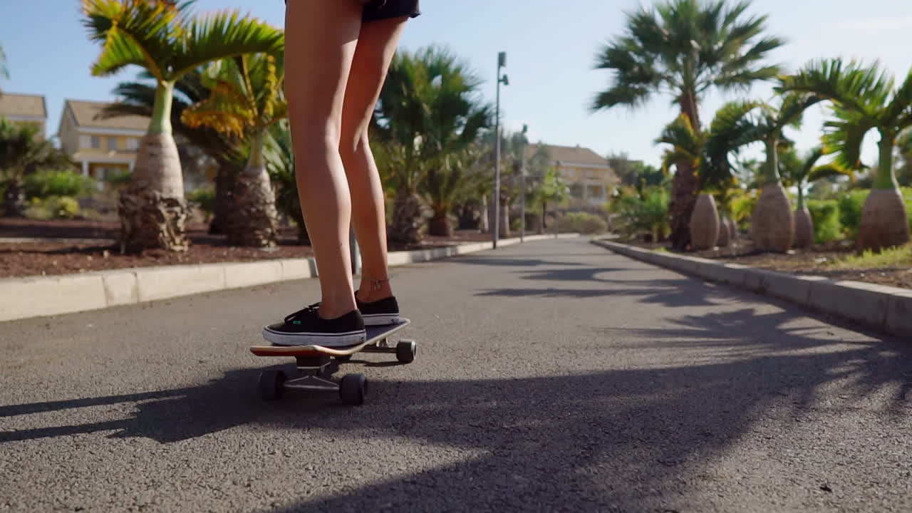 Slow motion captures the elegance as a young girl rides her longboard on the road beside the palm trees and beach