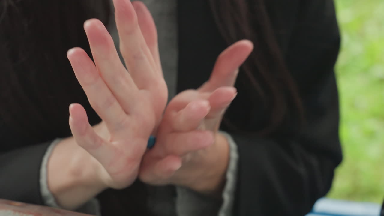 Hands preparing fingers with gentle rubbing, outdoor closeup of woman in jacket performing calming finger exercise on table, focused preparation ritual, subtle nervous energy, repetition and dexterity
