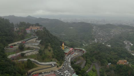 Aerial-view-towards-passage-leading-to-lush-decorative-mountain-temple---statue-outside-Taipei,-China