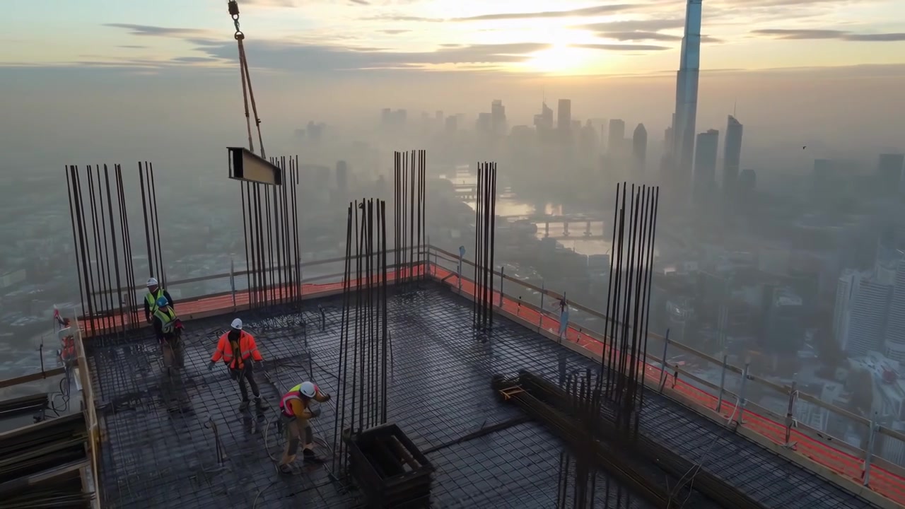 Construction Workers on Skyscraper Rooftop with Crane Lifting Steel Beam at Sunrise