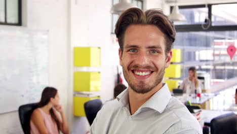 Young-white-man-in-office-walks-into-focus-and-smiles