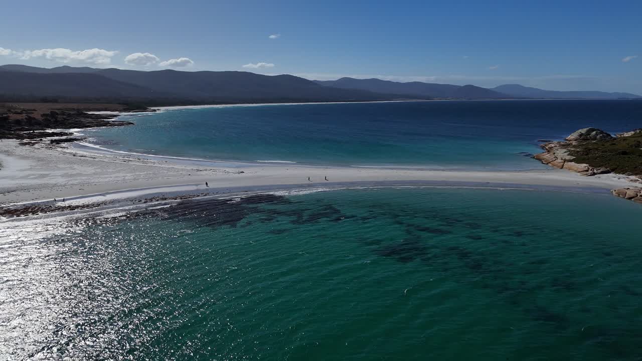 White sand beach with walking tourists at sandbar revealing Diamond Island, aerial dynamic