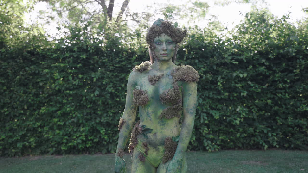 disparo medio de un modelo femenino con pintura corporal verde caminando y bailando lentamente en la naturaleza, en el estilo de las formas inspiradas en la naturaleza