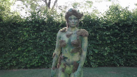 medium shot of a female model wearing green bodypaint walking and dancing slowly in nature, in the style of nature-inspired forms