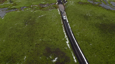 Aerial:-Panoramic-view-of-on-white-car-passing-through-a-puddle-of-water-on-muddy-road-partially-covered-with-snow