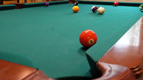 8 ball pool table where orange striped 13 ball is shot into the corner pocket closeup with several balls left on a brunswick with green felt or cloth using follow spin on the cue ball, low angle