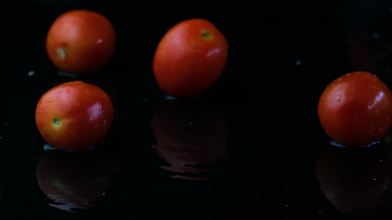 Three cherry tomatoes slowly dropping into frame joining three more already sitting in the shallow water