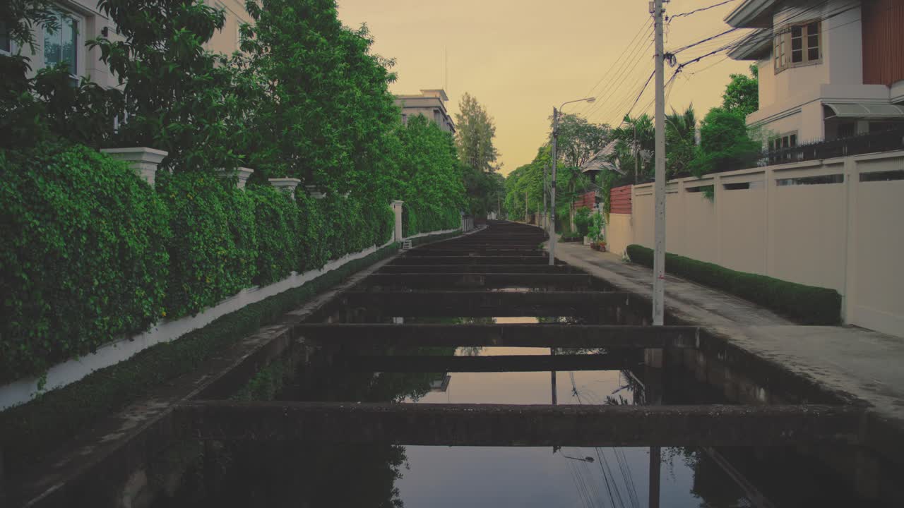 A tranquil scene of a canal behind residential homes, framed by lush greenery and captured during the warm hues of golden hour, exuding a peaceful and calming atmosphere.