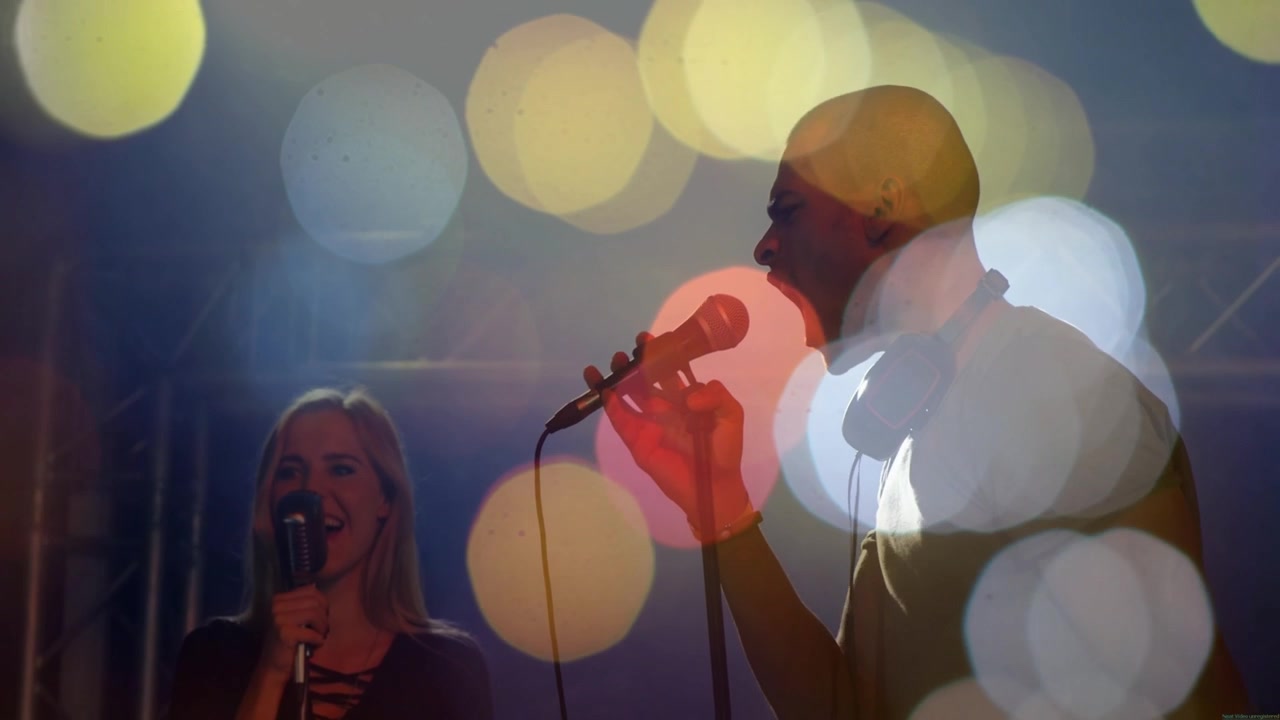 Mannlig sanger synger i håndholdt mikrofon, kvinnelig sanger blir med, bokeh-lys forsterker musikkduetten.