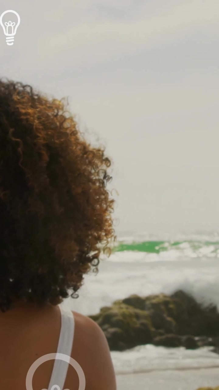 Animation of light bulb icons over african american woman by seaside