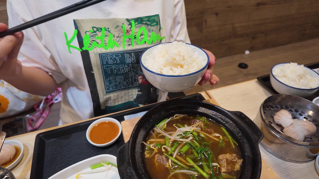 Close-up of person holding rice bowl and chopsticks over beef soup in Bangkok, Thailand.