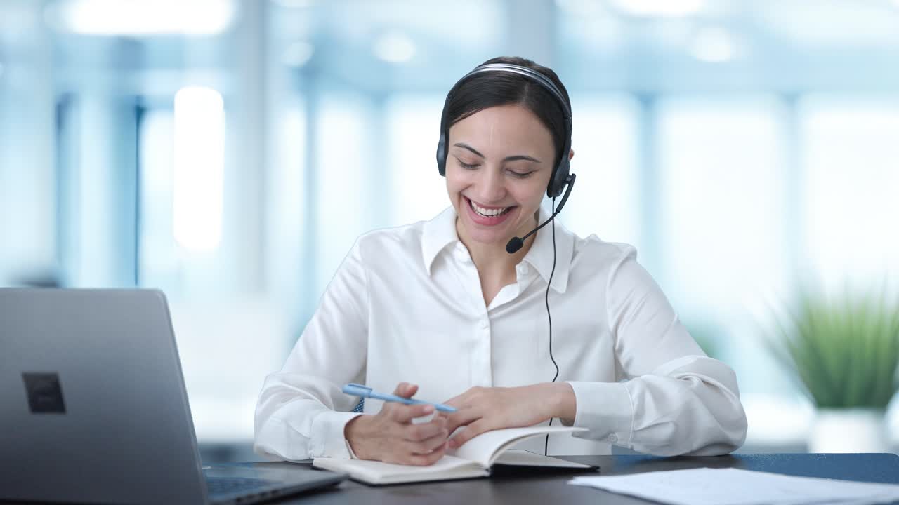 Operatrice indiana felice del call center che parla con il cliente e prende appunti.