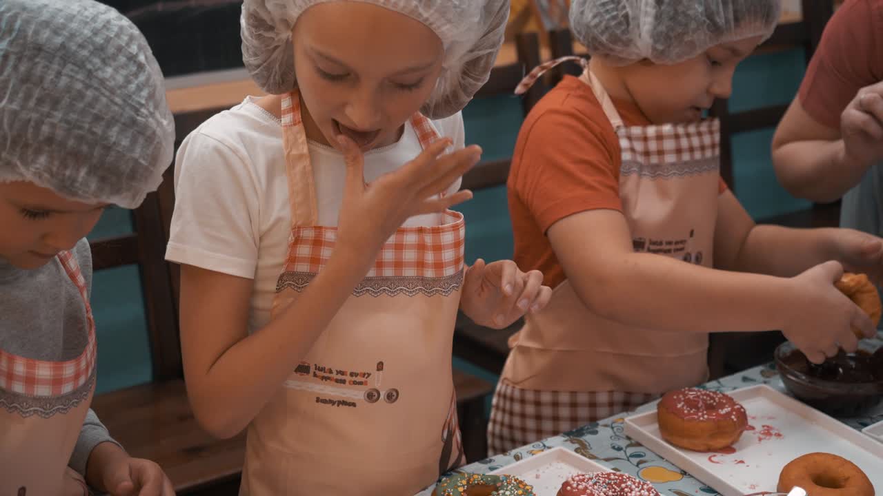 Children topping donuts on cooking master class in culinary school. Teenagers cooking donuts with colorful glaze in bakery master class. Cooking lesson in school.