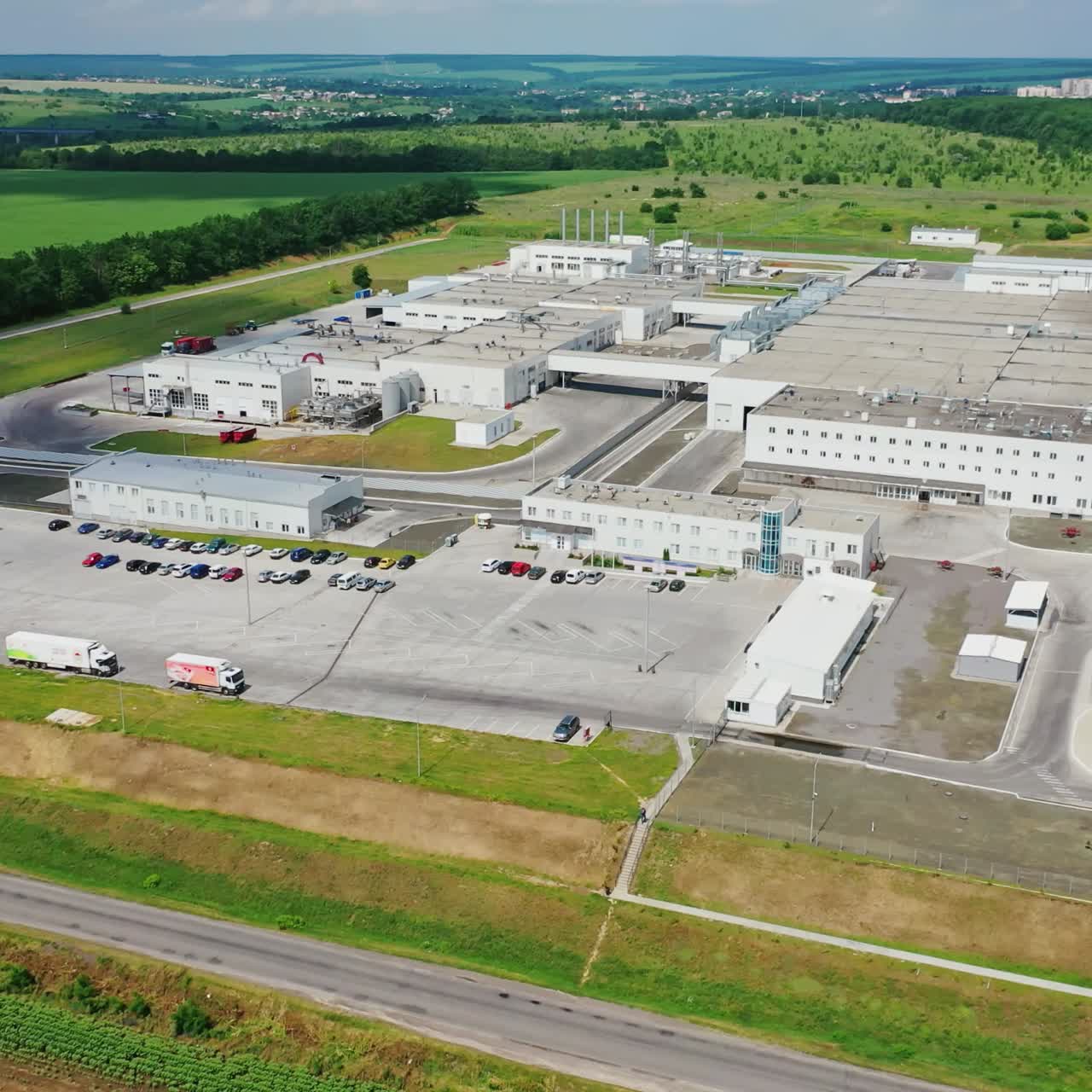 Manufacturing area on nature background. Modern industrial plant with cars parking surrounded by green fields. Aerial view.