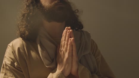 studio portrait of man wearing robes with long hair and beard representing figure of jesus christ praying