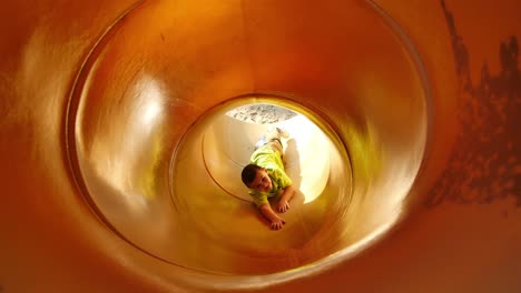 little boy in bright green shirt tries to climb back up yellow tube slide