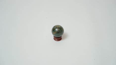 Small-Luxury-Stone-Granit-Ball-Sphere-on-Small-Walnut-Wooden-Base-Against-White-Background