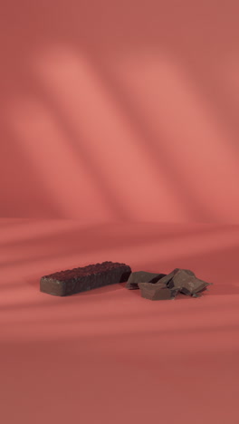 a close-up of a hand placing a dark chocolate-coated protein bar next to broken milk chocolate pieces on a soft coral pink background, highlighting a clean, minimal fitness aesthetic.