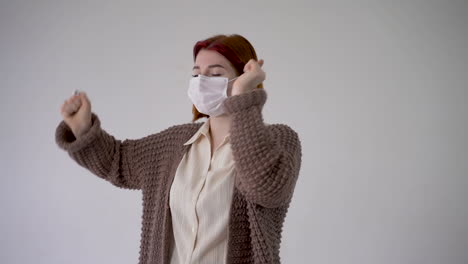 mujer joven y alegre bailando y usando una máscara médica. copia espacio y fondo blanco.