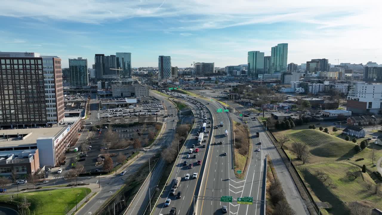 Pemandangan udara dari drone yang memperlihatkan jalan raya yang ramai di Nashville di bawah sinar matahari yang cerah, dengan lalu lintas yang stabil menuju kaki langit pusat kota, menunjukkan pertumbuhan perkotaan, jalan, dan kota modern di Tennessee, Amerika Serikat
