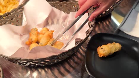 a hand uses tongs to serve crispy fried onion rings onto a black plate at a korean bbq restaurant