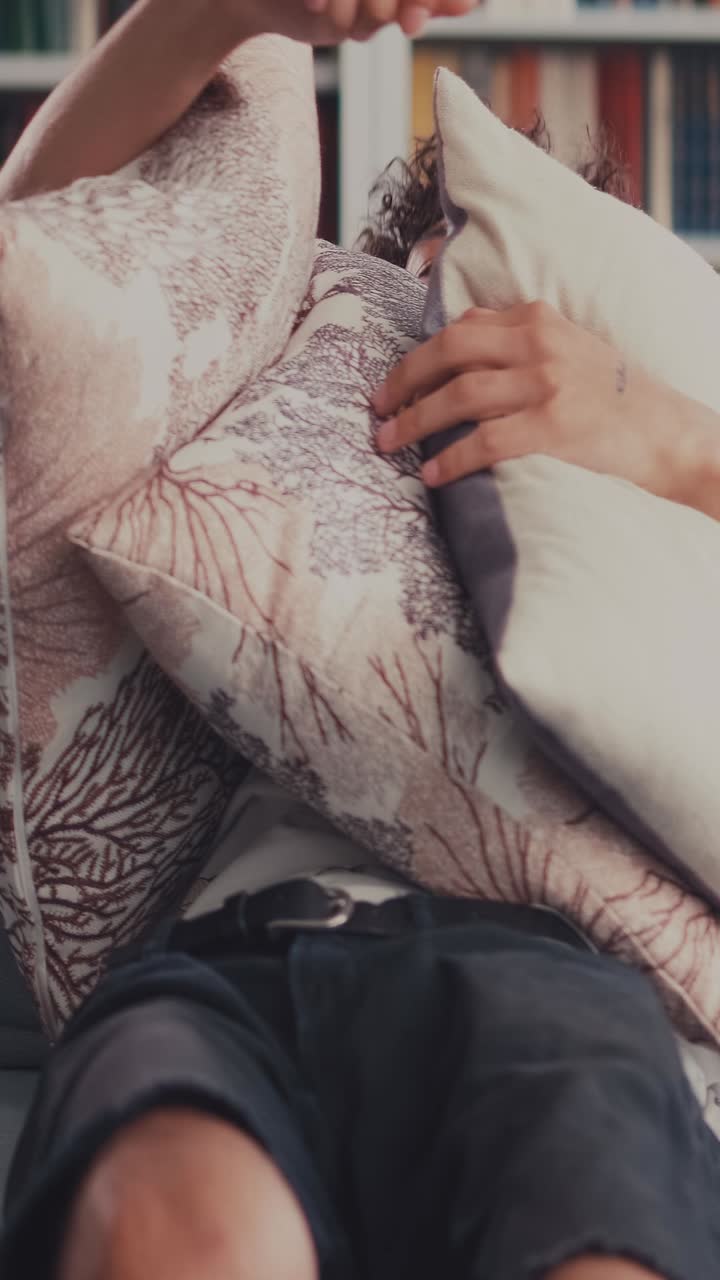 Young man relaxing on couch surrounded by cushions in cozy setting
