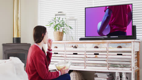 mujer caucásica viendo la televisión con un jugador de rugby afroamericano con la pelota en la pantalla