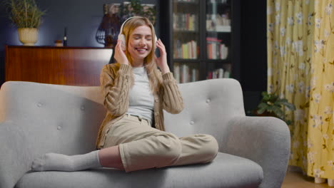 happy young woman listening music in wireless headphones while sitting on a couch at home 1