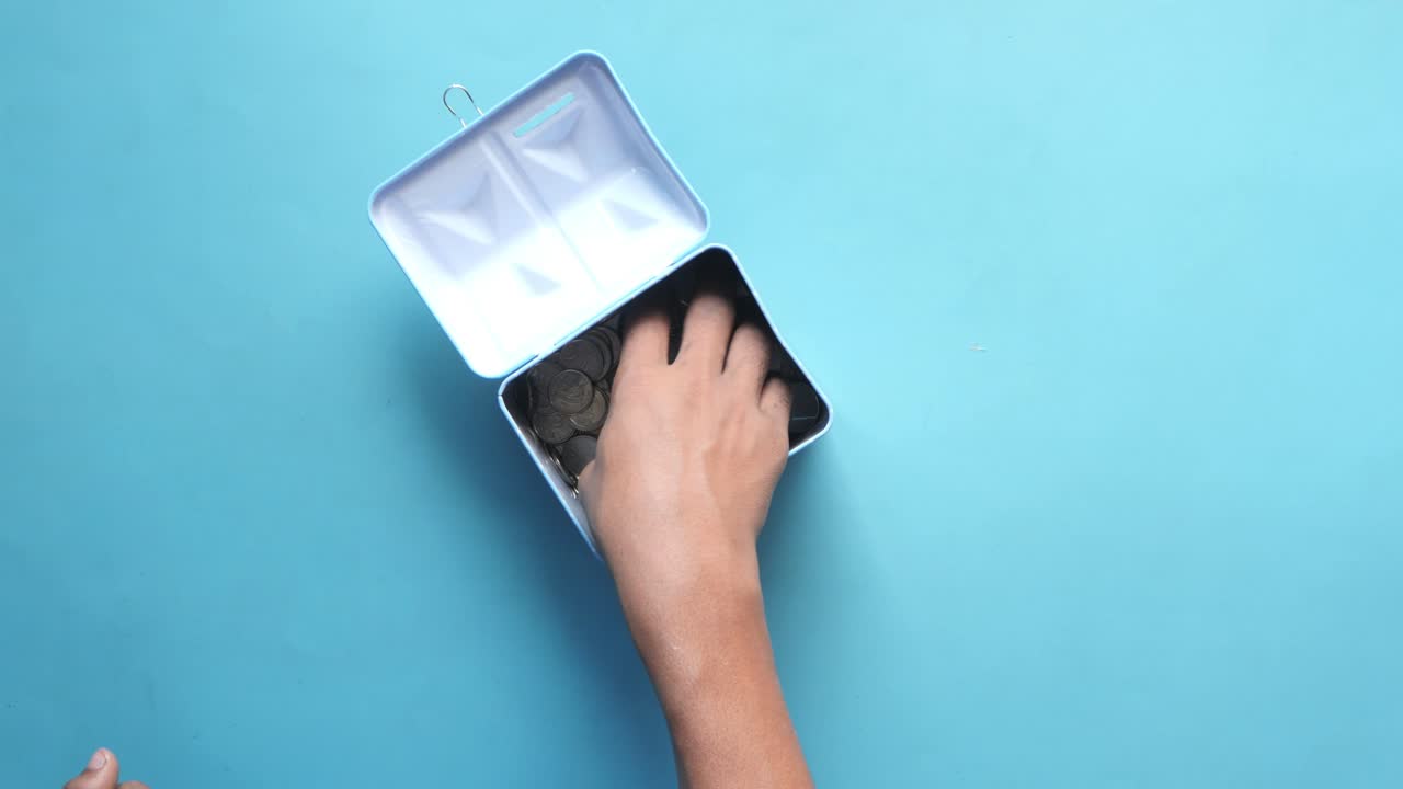 la mano poniendo monedas en una alcancía azul