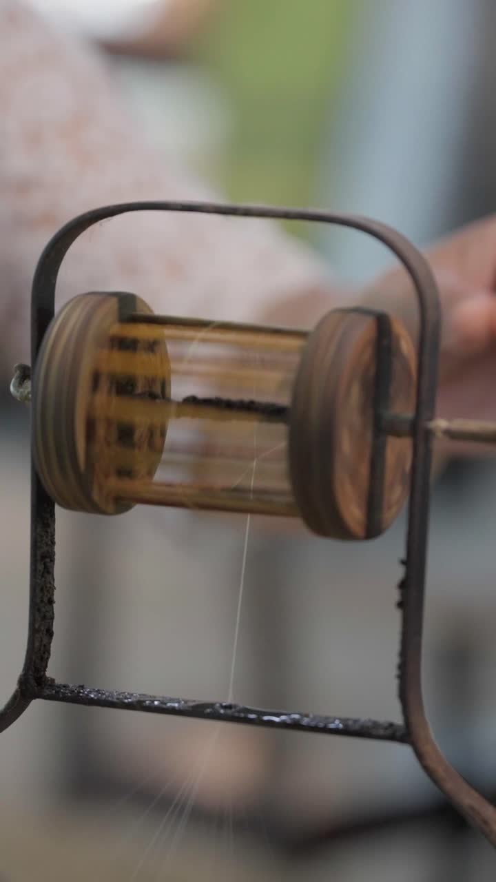 Close shot slow motion of fine silk threads pulling up a spent cocoon during reeling in traditional Thai sericulture delicate natural fiber work