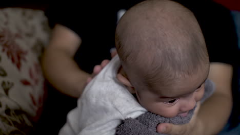 padre frotando suavemente a su hijo de 2 meses en la espalda para ayudarlo a eructar después de beber leche en su regazo