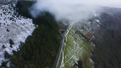 journey through wicklow: aerial tracking of a black car amidst misty mountains and snow-covered forests driving into the clouds