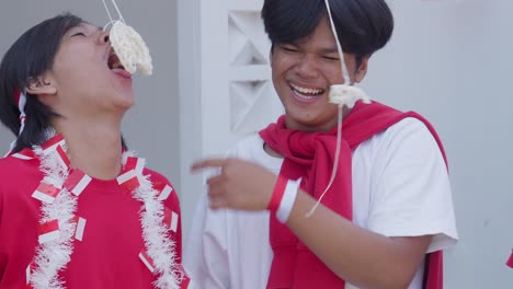 young asian friends having fun in crackers eating competition called lomba makan kerupuk on indonesian independence day celebration