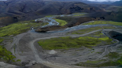 revealing drone footage of an off-road track leading to a river system in a valley with mountains in backdrop in the highlands of iceland