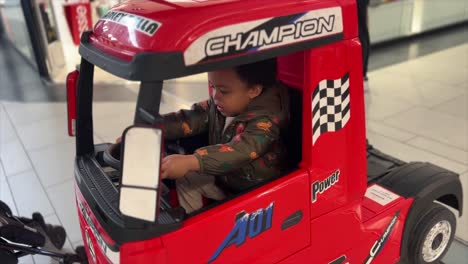 cute and exotic two-year-old black baby, mix raced, riding a big red toy truck inside a mall