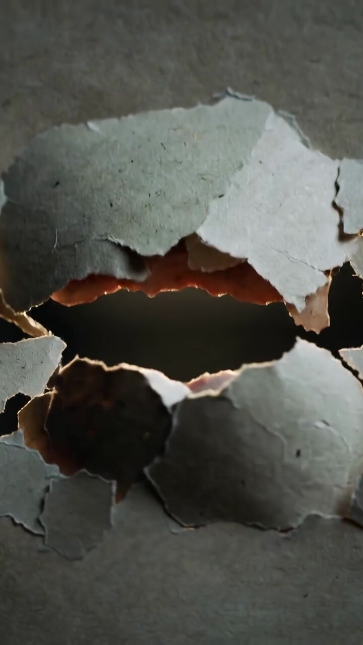 Vertical video: Shifting backlight revealing torn gray sheet in closeup, showing brown inner layer
