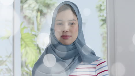 animation of light spots over biracial woman in hijab looking at camera