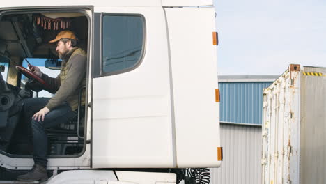 lavoratore che indossa giubbotto e berretto che organizza una flotta di camion in un parco logistico mentre parla al telefono in un camion