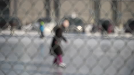 toma abstracta de personas patinando en una pista de hielo al aire libre a través de una valla metálica