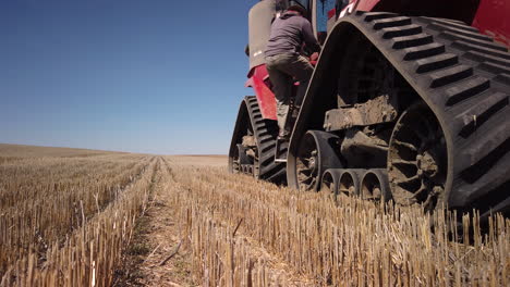 un joven agricultor caucásico molesto sale de una gran máquina tractora roja y arroja un sombrero al suelo y patea las ruedas con disgusto por el equipo roto, un cierre estático