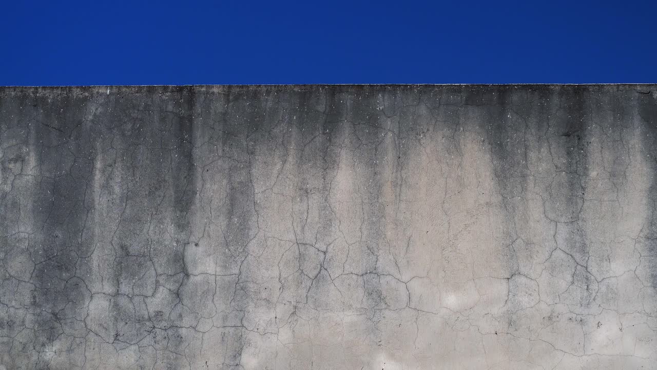 Rippling water reflections from a pool on a dirty white wall under a clear blue sky