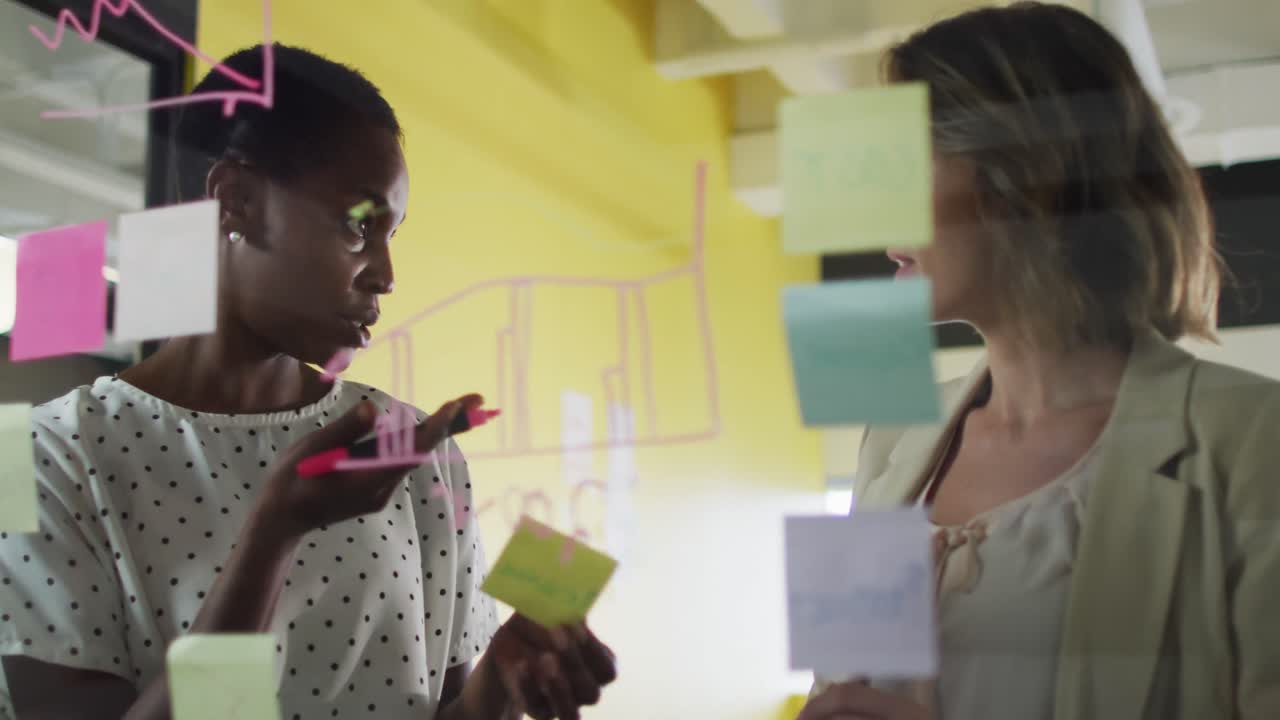 Two diverse female colleagues making notes and discussing at work