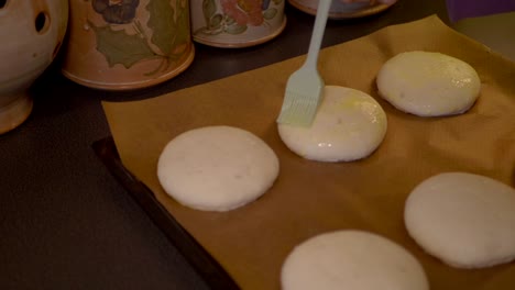 Una-Hembra-Cepillando-Un-Huevo-Limpio-Encima-De-Los-Bollos,-Preparándolos-Para-El-Horno